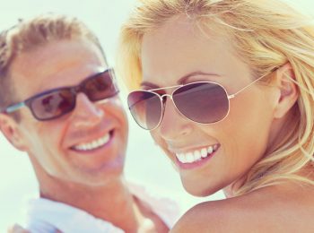 Instagram style photograph of happy and attractive man and woman couple wearing sunglasses and smiling in sunshine at the beach